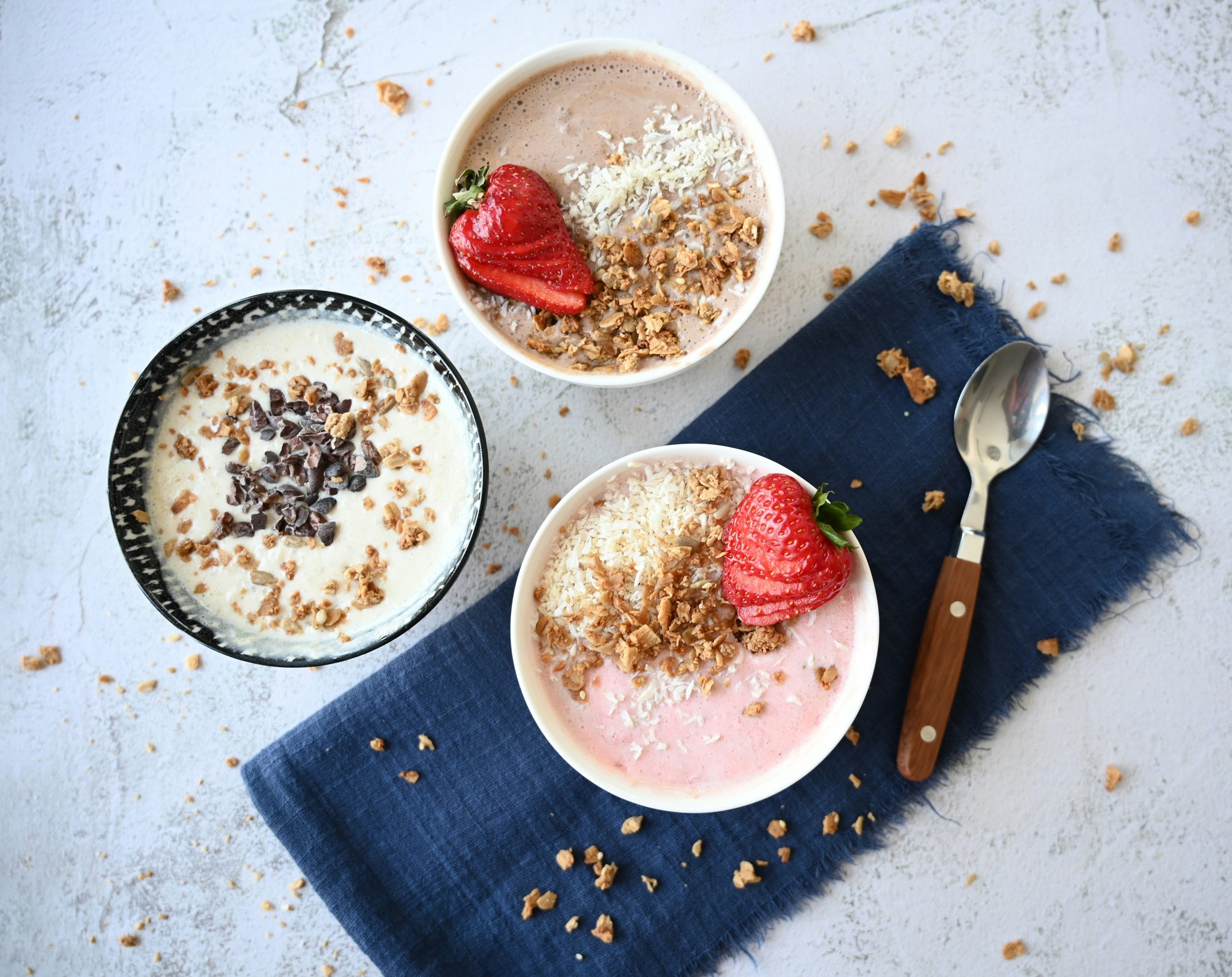 Drei Smoothie-Bowls mit Granola, Kokosraspeln und frischen Erdbeeren